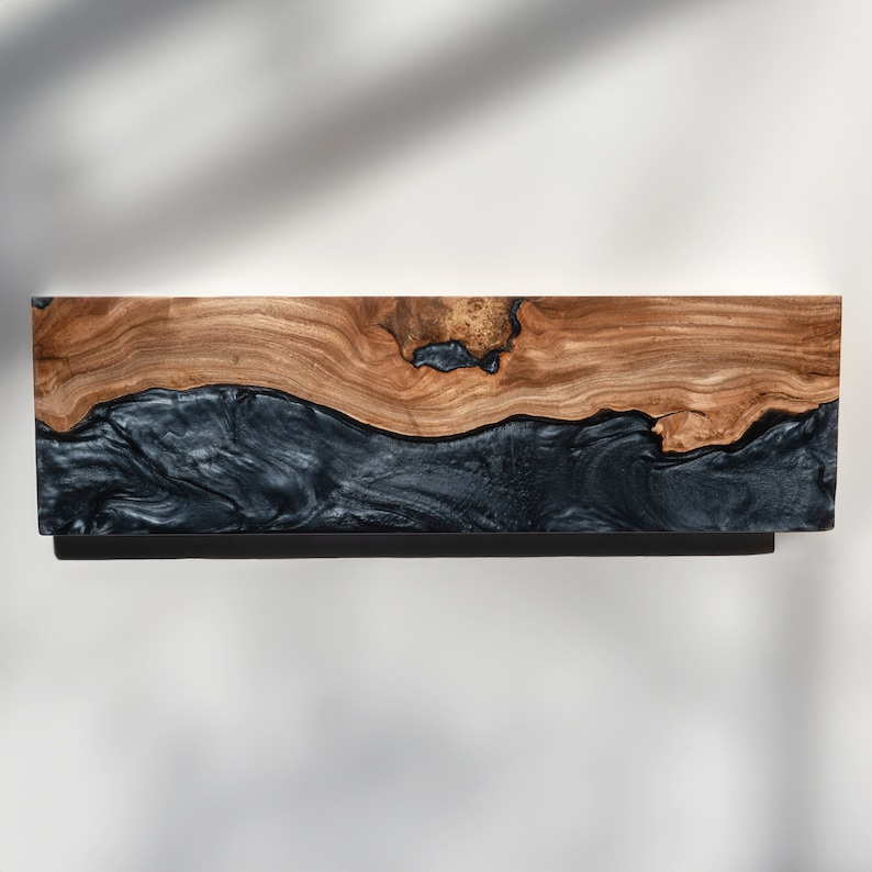 Puede incluir: Un estante de pared rectangular que presenta una secci&oacute;n superior de madera natural de color marr&oacute;n claro con un nudo prominente y una secci&oacute;n inferior contrastante de resina negra lisa con una textura veteada y arremolinada.