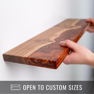 May include: A rectangular wooden shelf with a natural wood grain finish and a section of reddish-brown resin. The shelf is being held up against a white wall. The text "OPEN TO CUSTOM SIZES" is displayed on a gray banner.