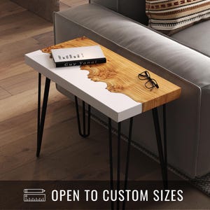 Może przedstawiać: Nowoczesny stolik boczny z białym i drewnianym blatem, wsparty na czarnych nogach typu hairpin. Na stole książka, okulary i napis "OPEN TO CUSTOM SIZES". Usłojenie drewna ma unikalny, naturalny wzór.