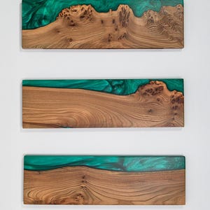 Puede incluir: Tres tablas rectangulares de madera natural con vetas y nudos pronunciados, cada una con una incrustaci&oacute;n de resina verde esmeralda transl&uacute;cida y lisa a lo largo de un borde largo que crea un efecto visual fluido y ondulado en la superficie.