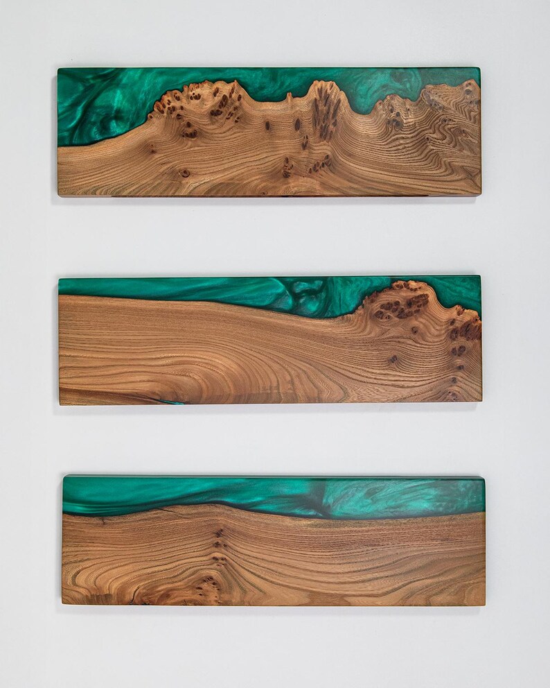 Puede incluir: Tres tablas rectangulares de madera natural con vetas y nudos pronunciados, cada una con una incrustaci&oacute;n de resina verde esmeralda transl&uacute;cida y lisa a lo largo de un borde largo que crea un efecto visual fluido y ondulado en la superficie.