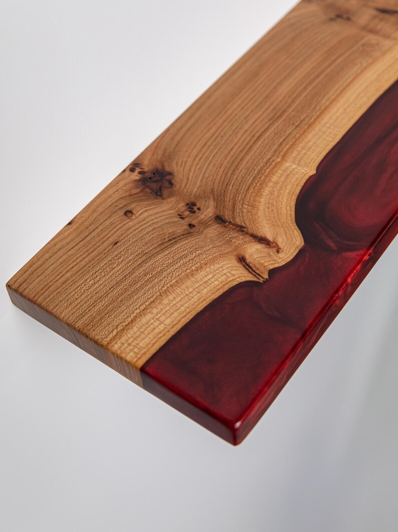 Puede incluir: Una tabla de servir rectangular que presenta una secci&oacute;n de madera de color marr&oacute;n claro natural con nudos visibles en un lado y una secci&oacute;n de resina roja transl&uacute;cida profunda y lisa en el otro, unidas por un patr&oacute;n org&aacute;nico ondulado a lo largo.