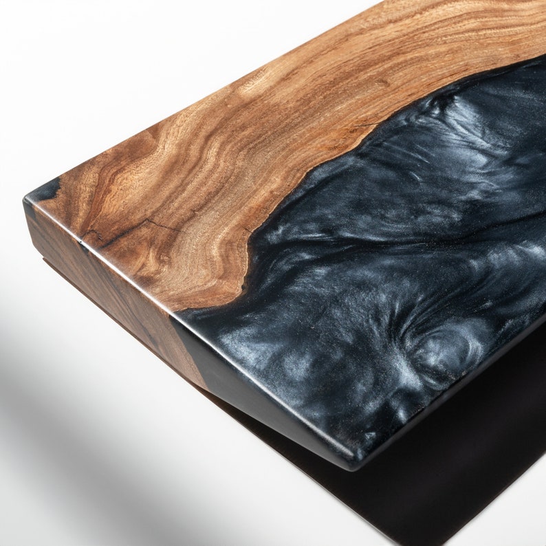 Puede incluir: Una tabla de servir rectangular que presenta una secci&oacute;n de madera natural con vetas marrones visibles y una secci&oacute;n contrastante de resina negra lisa con una textura arremolinada y nacarada que imita la apariencia de agua fluyendo.