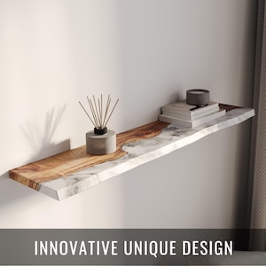 Puede incluir: Una estantería flotante con un diseño único, que combina madera y mármol. La estantería está adornada con una pequeña vela gris, una pila de libros y un difusor de cañas. El texto "INNOVATIVE UNIQUE DESIGN" se muestra debajo.