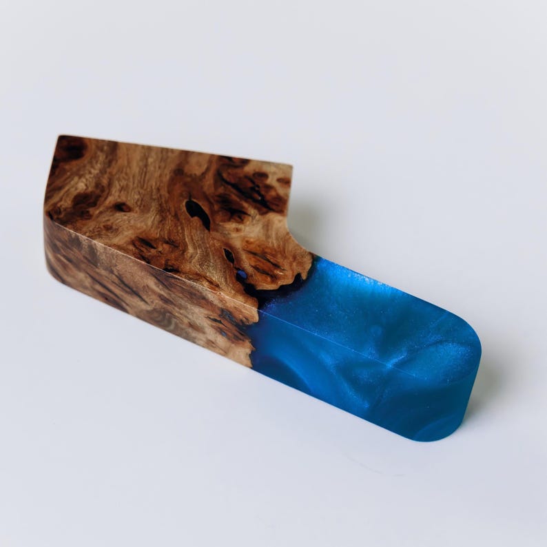 Op de afbeelding: Een handgemaakt houten kaasmes met een opvallend ontwerp. De handgreep is gemaakt van rijk generfd hout, dat overgaat in een levendig blauw harsblad. Dit unieke stuk combineert natuurlijke en moderne elementen.