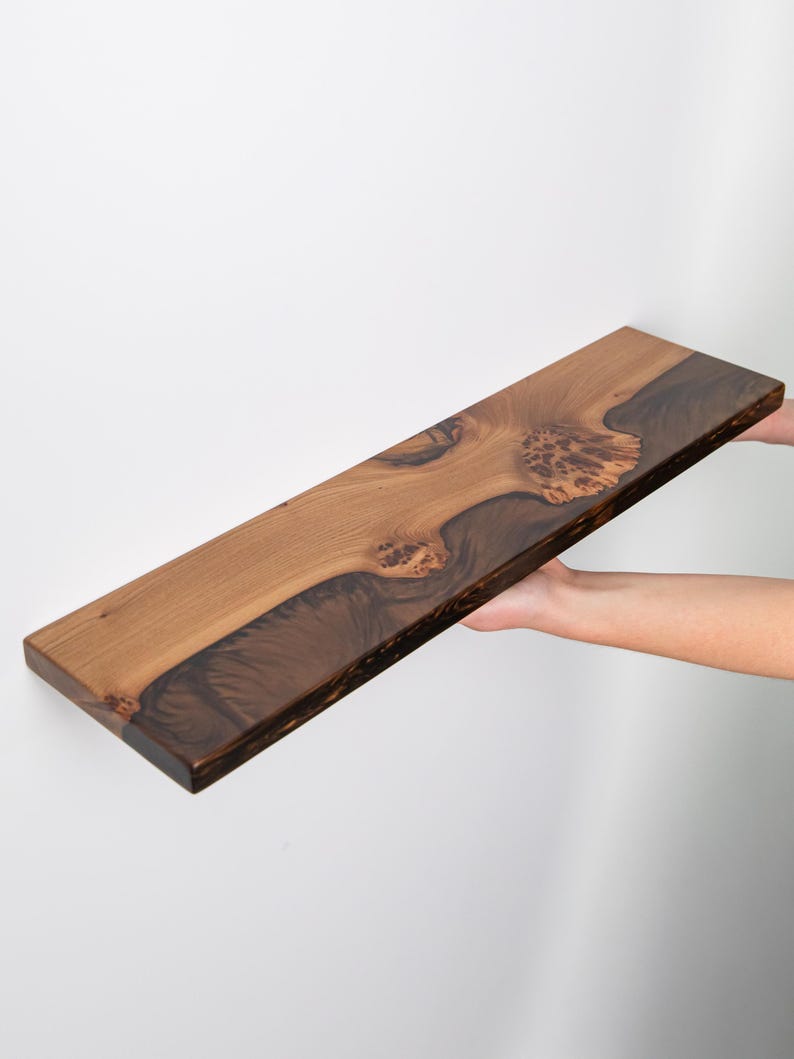 Puede incluir: Un estante flotante rectangular de madera con un dise&ntilde;o de borde natural. La madera muestra un patr&oacute;n de veta contrastante con secciones de color tostado claro y detalles de madera nudosa de color marr&oacute;n oscuro en la superficie.