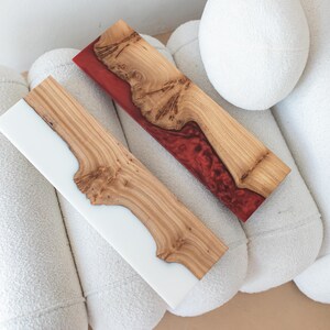 Puede incluir: Dos tablas de servir rectangulares hechas de madera natural con bordes irregulares. Una tabla presenta una secci&oacute;n de resina blanca s&oacute;lida, mientras que la otra tiene una secci&oacute;n de resina roja transl&uacute;cida. Ambas muestran vetas de madera.