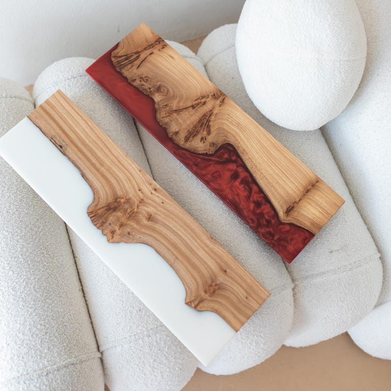 Puede incluir: Dos tablas de servir rectangulares hechas de madera natural con bordes irregulares. Una tabla presenta una secci&oacute;n de resina blanca s&oacute;lida, mientras que la otra tiene una secci&oacute;n de resina roja transl&uacute;cida. Ambas muestran vetas de madera.