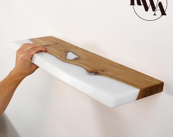 May include: A rectangular wall shelf featuring a combination of natural light brown wood with visible grain and a smooth, opaque white resin section. The wood has a central knot filled with white resin. The logo RWA is in the corner.