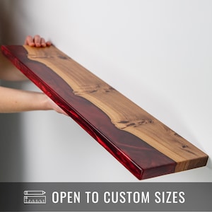 May include: A wooden shelf with a red resin edge and a natural wood grain centre. The shelf is held against a white wall. The text "OPEN TO CUSTOM SIZES" is displayed at the bottom. The shelf is likely customisable.