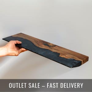 Puede incluir: Un estante rectangular que combina madera marr&oacute;n natural con un patr&oacute;n de veta prominente y una secci&oacute;n de resina negra s&oacute;lida y lisa que fluye a trav&eacute;s de la superficie en una forma org&aacute;nica irregular con un borde plano.