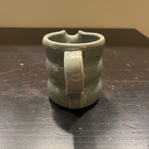 K&ouml;nnte beinhalten: Ein kleiner, hellblauer Keramik-Krug mit einer strukturierten Oberfl&auml;che und einem Henkel. Der Krug hat eine leicht abgerundete Form und eine breite &Ouml;ffnung.