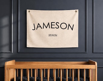 Peut inclure: Une bannière murale rectangulaire en tissu beige avec le nom JAMESON en grandes lettres capitales noires légèrement arquées, et le nom IRWIN en plus petites lettres capitales noires en dessous. La bannière possède deux œillets métalliques.