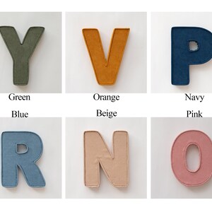 May include: A collection of fabric letters in various colors: green, orange, navy, blue, beige, and pink. Each letter is displayed against a white background, with the color name below each letter.