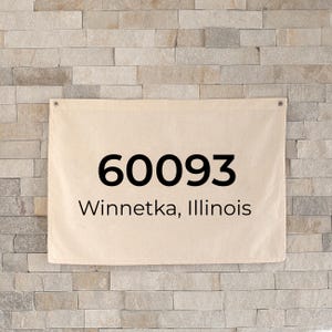 Może przedstawiać: Beżowy baner z płótna z czarnym tekstem "60093 Winnetka, Illinois" jest wyświetlany na tle jasnobrązowej kamiennej ściany. Baner ma przelotki w rogach do zawieszenia.