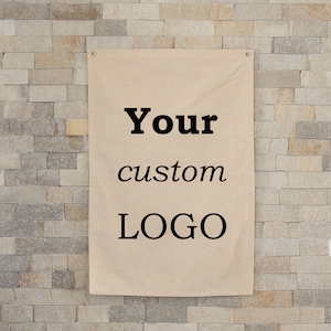 May include: Tan banner with the words "Your custom LOGO" in black, hanging against a light-colored brick wall. The banner has grommets at the top for hanging.