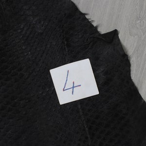 May include: A close-up of a black leather material with a textured pattern. A white note with the number "4" written on it is in the lower right corner of the image.