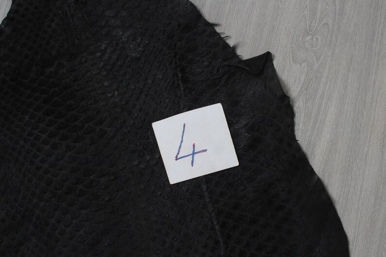 May include: A close-up of a black leather material with a textured pattern. A white note with the number "4" written on it is in the lower right corner of the image.