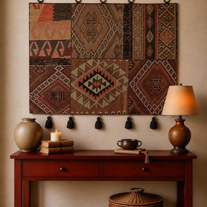 Pode incluir: Uma tapeçaria retangular composta por um mosaico de painéis de tecido entrelaçado com padrões geométricos em tons de castanho, laranja e preto, suspensa por cinco anéis metálicos e rematada com cinco borlas castanho-escuras na extremidade inferior.