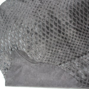 May include: A piece of black snakeskin leather with a textured pattern. The leather is folded in half and has a rough, unfinished edge.