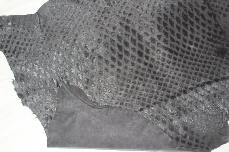 May include: A piece of black snakeskin leather with a textured pattern. The leather is folded in half and has a rough, unfinished edge.