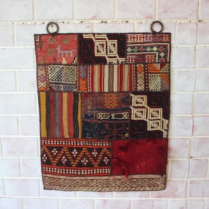Può includere: Un tappeto patchwork colorato con motivi geometrici in tonalità di rosso, marrone, blu e bianco. Il tappeto è realizzato in tessuto tessuto e ha un bordo con frange.