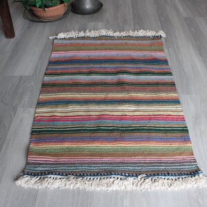 May include: A colorful striped rug with a fringe border. The rug has a variety of colors, including red, blue, green, and brown.
