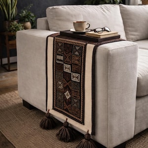 May include: A white ceramic mug with a black handle and the text "But First, Coffee" in a bold, black font. The mug is set against a blurred background, suggesting a cozy setting.