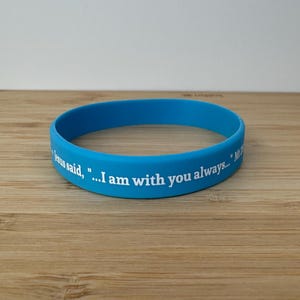 May include: A blue silicone wristband with the text "Jesus said, ...I am with you always..." in white.