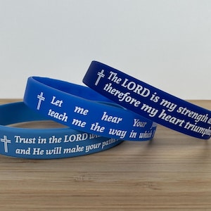 May include: Three blue silicone wristbands with white cross and inspirational text. The text on the wristbands reads: "The LORD is my strength and therefore my heart triumphs", "Let me teach me the way in which you hear your", and "Trust in the LORD with all your heart and He will make your paths straight."