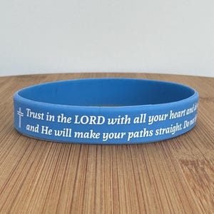 May include: A blue silicone bracelet with the text "Trust in the LORD with all your heart and do and He will make your paths straight. Do not" in white.