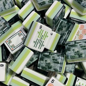 May include: A collection of rectangular mahjong tiles featuring a mix of green marbled backs and white faces. The faces display various markings including green bamboo stalks, circular target patterns, and numerical characters in black and green ink.