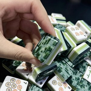 May include: A collection of rectangular mahjong tiles featuring a white face with circular patterns and numbers, and a dark green marbled back. The tiles have a layered design with a light green stripe between the white and dark green sections.
