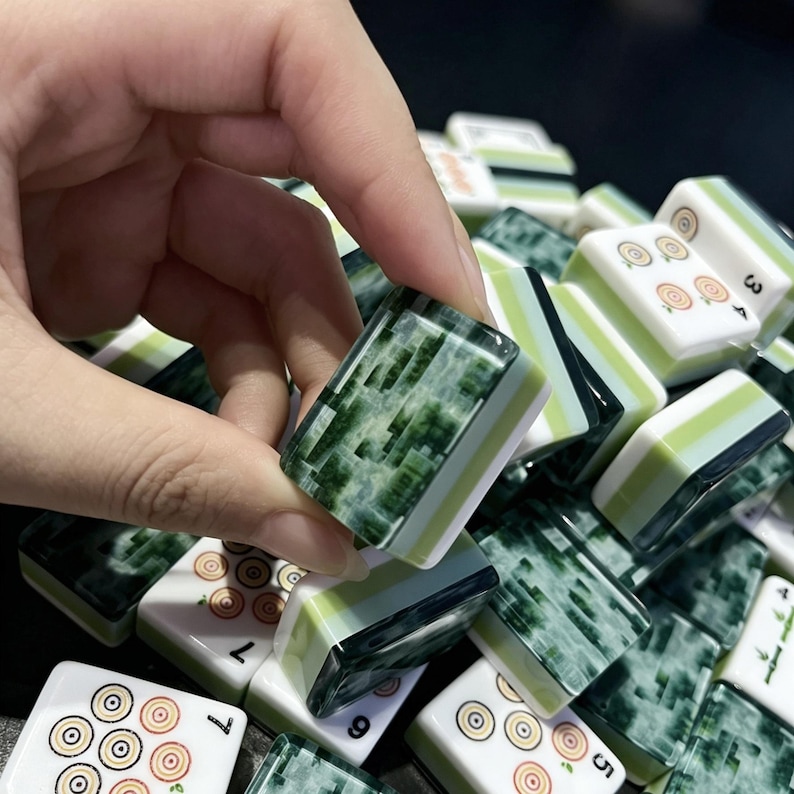 May include: A collection of rectangular mahjong tiles featuring a white face with circular patterns and numbers, and a dark green marbled back. The tiles have a layered design with a light green stripe between the white and dark green sections.