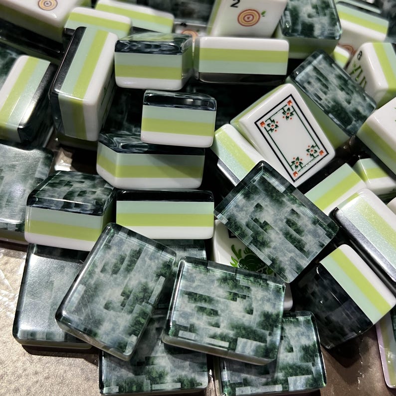 May include: A collection of rectangular mahjong tiles featuring a mix of designs. Some tiles display a tri-color pattern of white, light green, and dark green, while others show a dark green marbled texture or a white face with floral motifs.