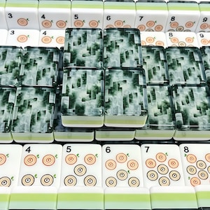 May include: A collection of mahjong tiles featuring white rectangular blocks with green and light green bases. Some tiles display numerical digits and circular wood grain patterns, while others feature a dark green and white marbled design.