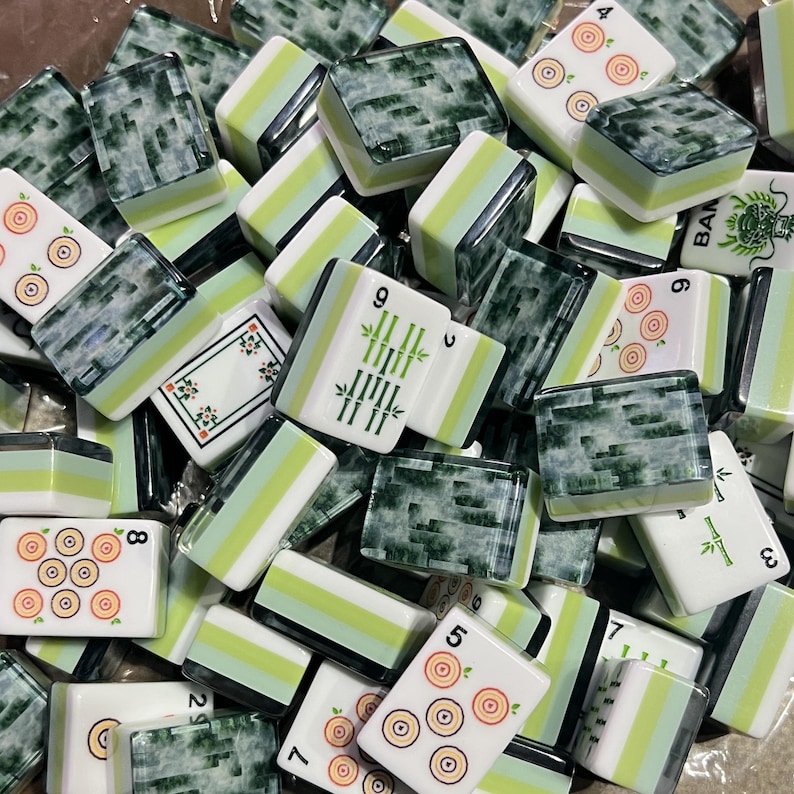 May include: A collection of rectangular mahjong tiles featuring a mix of green marbled backs and white faces. The faces display various markings including green bamboo stalks, circular target patterns, and numerical characters in black and green ink.