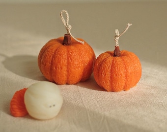 May include: Two orange pumpkin-shaped candles with a string wick and a smaller white pumpkin-shaped candle with a brown stem.