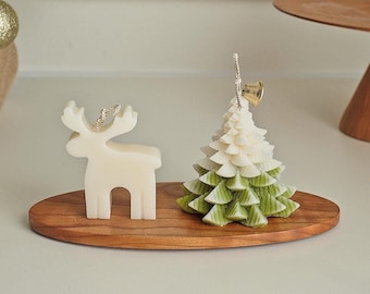 May include: A white reindeer and a green and white Christmas tree candle on a wooden oval tray.