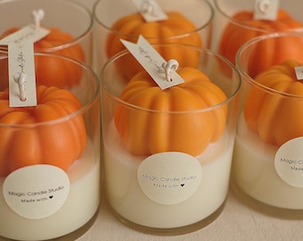 May include: Six glass jars with pumpkin-shaped candles inside. Each jar has a white label with the text "Magic Candle Studio Made with" on it.