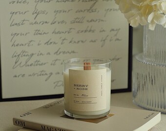 May include: A glass candle jar with a wooden wick and a label that reads "Berry + Rose" and "10hr". The candle is sitting on top of a stack of books with the words "OH MAGAZINE" and "Rayon de soleil" visible.