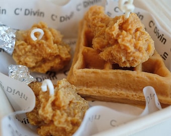 May include: A close-up of a waffle with fried chicken on top. The waffle is light brown and the chicken is golden brown. The waffle and chicken are in a white paper container with the words "C' Divin" printed on the paper.