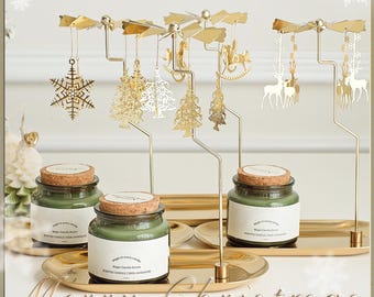 May include: A festive Christmas candle set with three glass jars of green scented candles, each with a cork lid. Above, a gold-colored carousel with decorative ornaments, including snowflakes, trees, and reindeer, spins above the candles. The words "Merry Christmas" are visible.