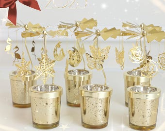 May include: Set of six gold metal candle holders with a carousel design. Each holder features a different decorative element, including butterflies, snowflakes, and stars. The holders are placed on a white surface.