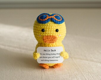 May include: A yellow crocheted duck wearing blue and orange goggles holds a white card with the text "Hello Duck. Do one thing today that you know you will regret not doing tomorrow."