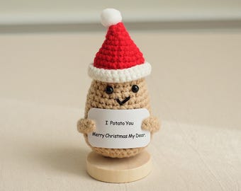 May include: A crocheted potato wearing a red and white Santa hat holds a sign that says "I Potato You Merry Christmas My Dear."
