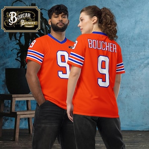 Op de afbeelding: Twee mensen dragen oranje voetbaltruien met blauwe en witte strepen. De trui aan de linkerkant heeft het nummer 9 op de voorkant. De trui aan de rechterkant heeft de naam "BOUCHER" en het nummer 9 op de achterkant.