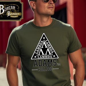Peut inclure: Un t-shirt vert avec un graphique blanc d'un triangle contenant le mot "Lambda". Le texte "Adams College '84" est écrit sous le triangle.