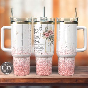 May include: White tumbler with a gold rim and a pink glitter design. The tumbler has a handle and a straw. The tumbler features a cross with pink flowers and the text "Fear not, I am with you, be not dismayed, I am your God. Strengthen then you, I will help you, I will uphold you with my righteous right hand.  Psalm 46:1".