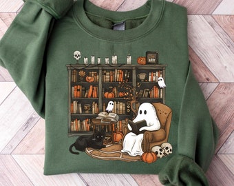 May include: A green sweatshirt with a spooky Halloween design featuring a ghost reading a book in a chair by a bookshelf filled with books. There are also black cats, pumpkins, and skulls in the design.